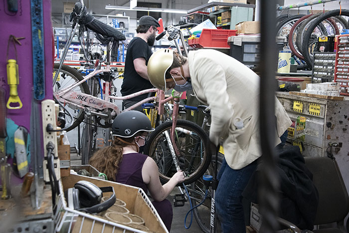 people wearing masks working on bicycles in a crowded shop