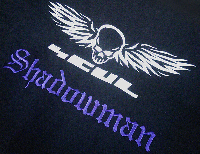 an embroidered piece of black wool with the SCUL logo and the word 'Shadowman' in old English letters in purple beneath it