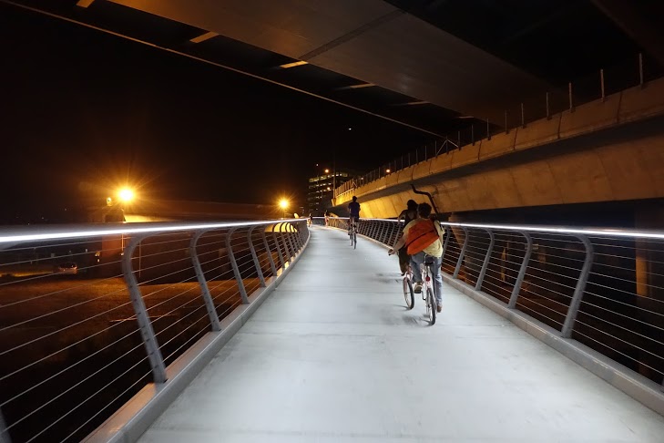 chopper bicycles riding up a sylish suspension pedestrian bridge at night
