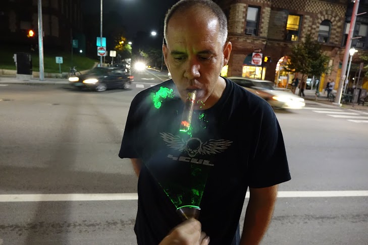 a man smokes a cigar while someone illuminates the smoke by quickly waving a green laser in front of him
