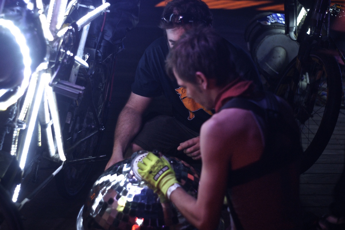 two people make repairs on a hollow disc ball on the street