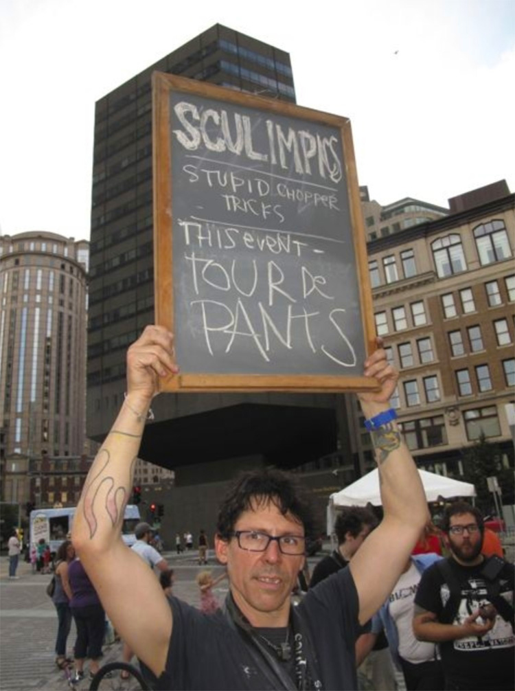 a man holding a chalkboard sign that reads 'SCULimpics' Stupid Chopper Tricks - This event - tour de pants